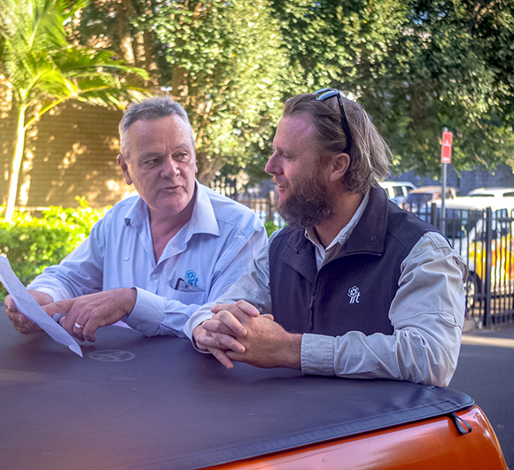 Two facilities management staff discussing the next job on bonnet of work truck